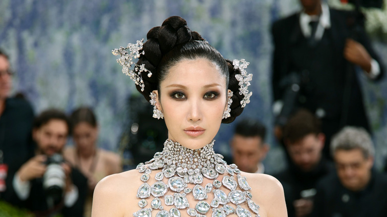 Ejae posing at the 2026 Met Gala in a crystal halter-top dress with her hair up and decorated with crystal accessories.