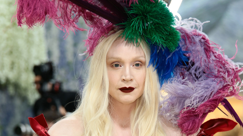 Gwendoline Christie posing at the 2026 Met Gala with her hair down wearing a large feather hat and dark red lipstick.
