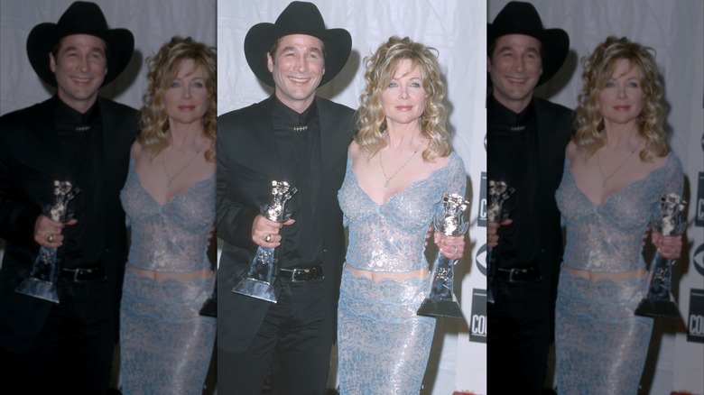 Clint Black wearing an all black outfit and Lisa Hartman Black wearing a shiny blue two-piece set at the 2000 ACM Awards.