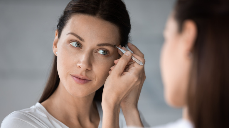 Woman tweezing eyebrow in mirror