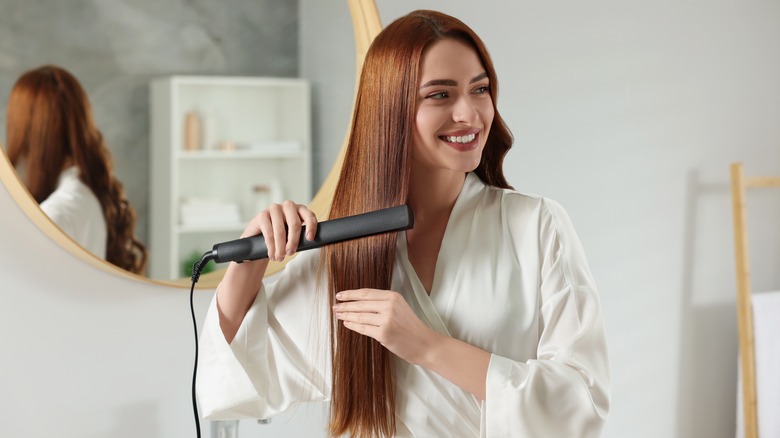 Woman using flat iron on hair in bathroom