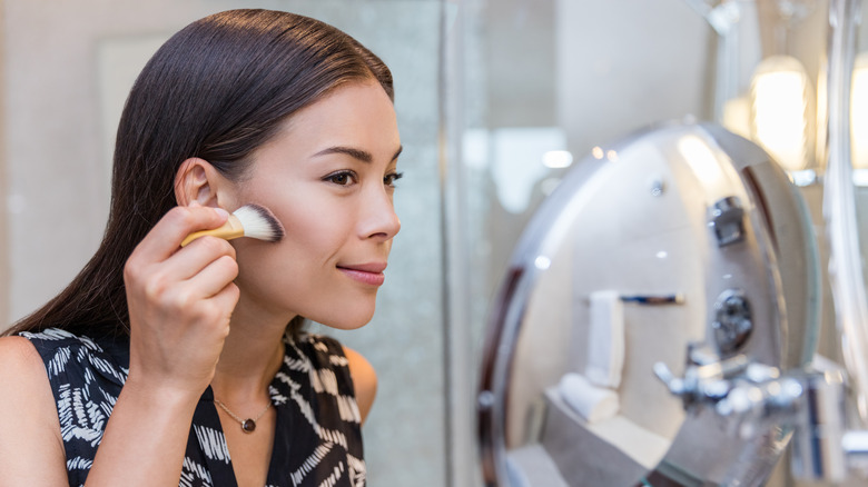 woman applying makeup to cheek 