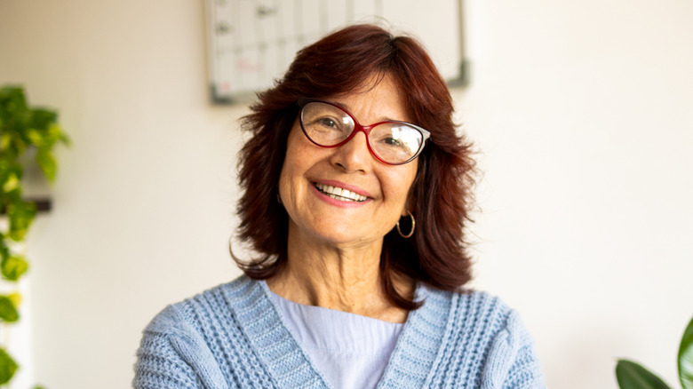 An odler woman with an auburn shag and glasses smiles