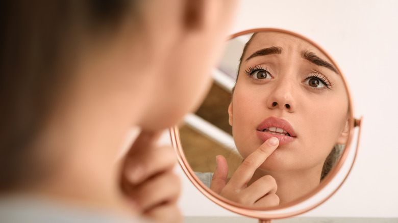 Young woman examines dry lips in mirror 