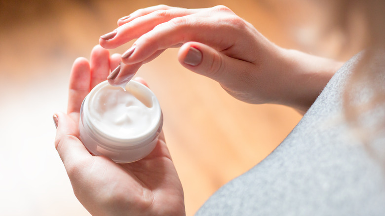 woman's fingers taking cream from jar
