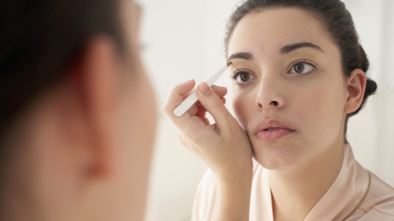 Woman plucking eyebrows in mirror