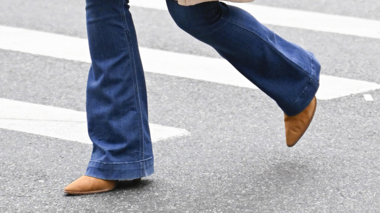A woman taking a step while wearing flared jeans and suede boots