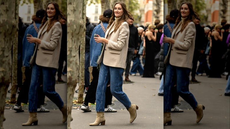 A woman wearing a tan blazer, jeans, and suede boots