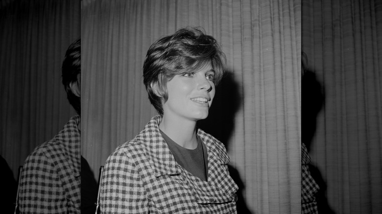 Katharine Ross smiles wearing a checked blazer and a pixie cut.