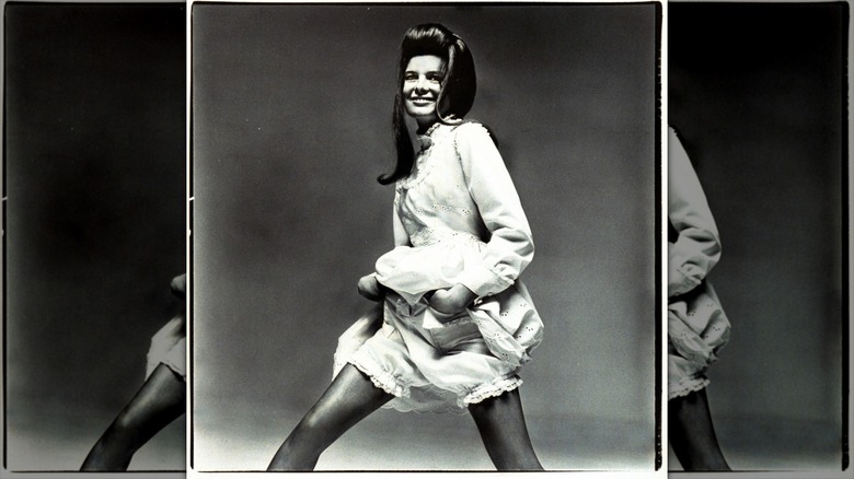 Katharine Ross holds up her pinafore and shows her frilled undergarments.