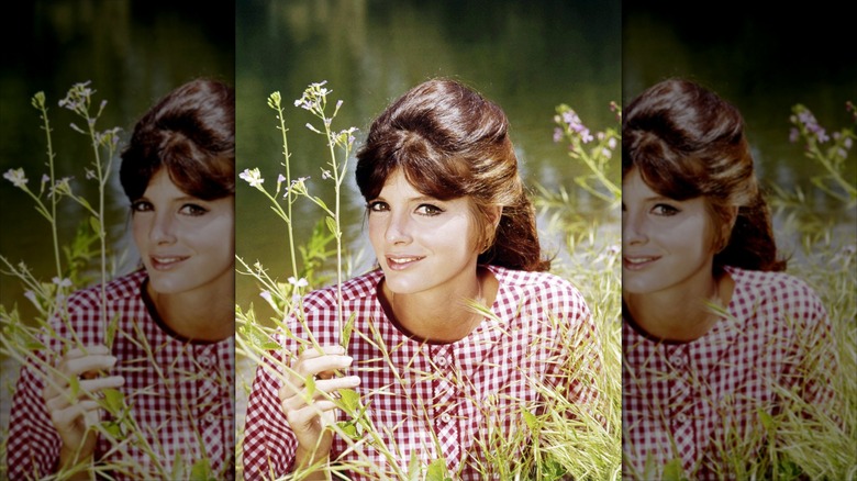 Katharine Ross smiles wearing a red-and-white gingham shirt.