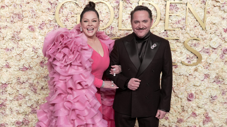 Melissa McCarthy and Ben Falcone walking the 2025 Golden Globes' carpet in a pink dress and a black suit, repsectively