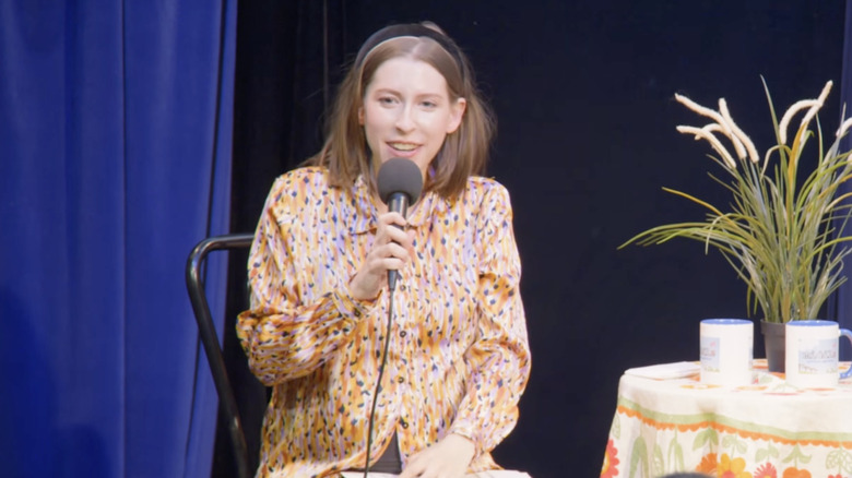 Eden Sher speaks into a microphone while on stage for a live show