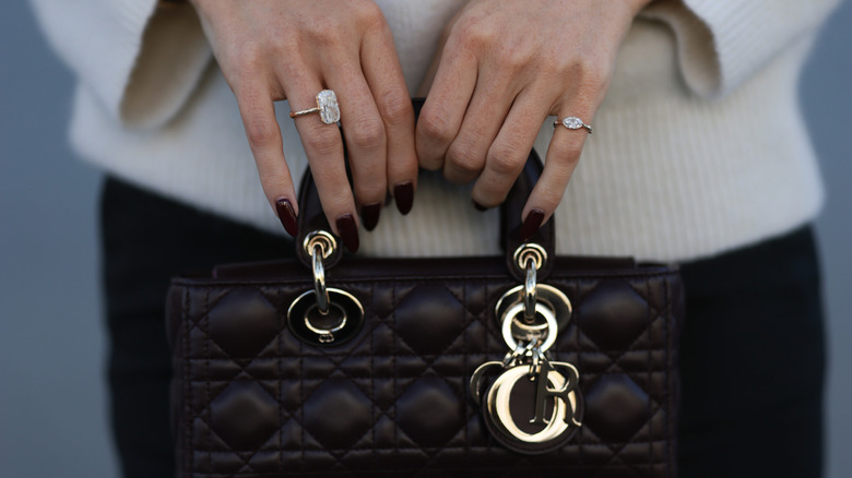 A woman with a Bordeaux manicure holding a purse