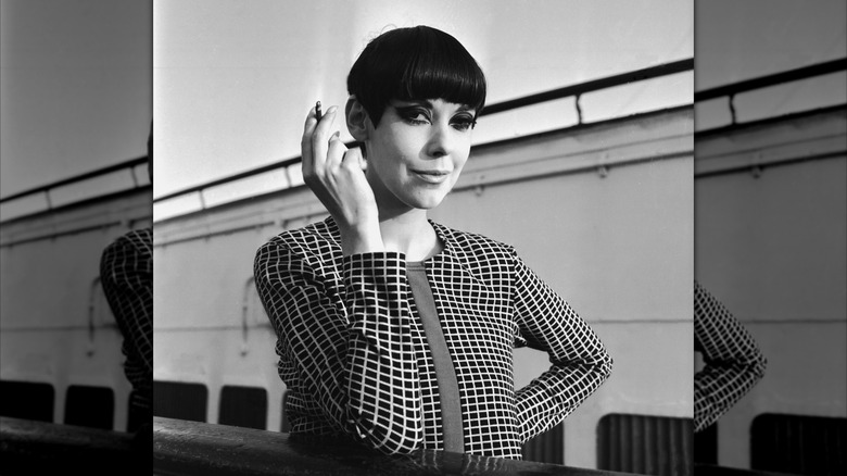 A portrait of Peggy Moffitt holding a cigarrette and smiling in black and white