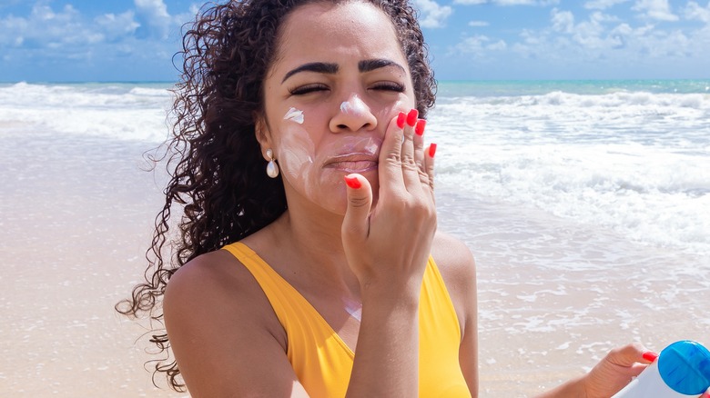 woman applying sunscreen to her face at the beach