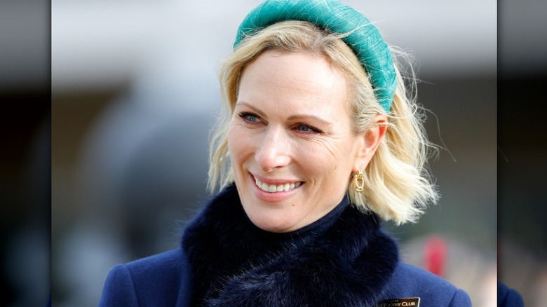 Zara Tindall smiles at an event, wearing a large green headband