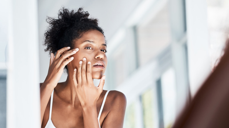 woman examining her face in mirror