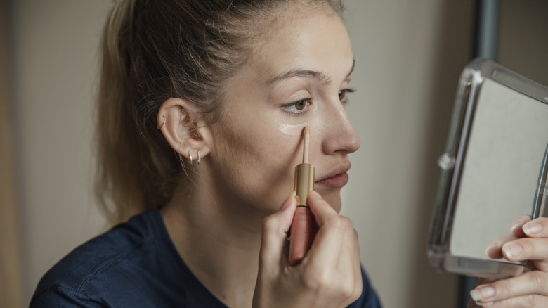 Woman applying concealer under eyes