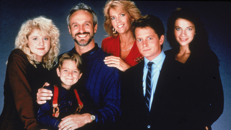 The cast of Family Ties poses for a family portrait in front of a dark blue backdrop.