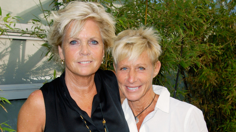 Meredith Baxter and wife Nancy Locke pose together in front of green foliage in the background.