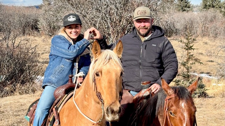 Amber and Shawn Marshall pose for a photo by creating a heart  with their hands during a horse ride