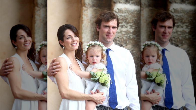 Michelle Morgan holding her daughter Mara with her husband Derek standing with his arm wrapped around her upper back.
