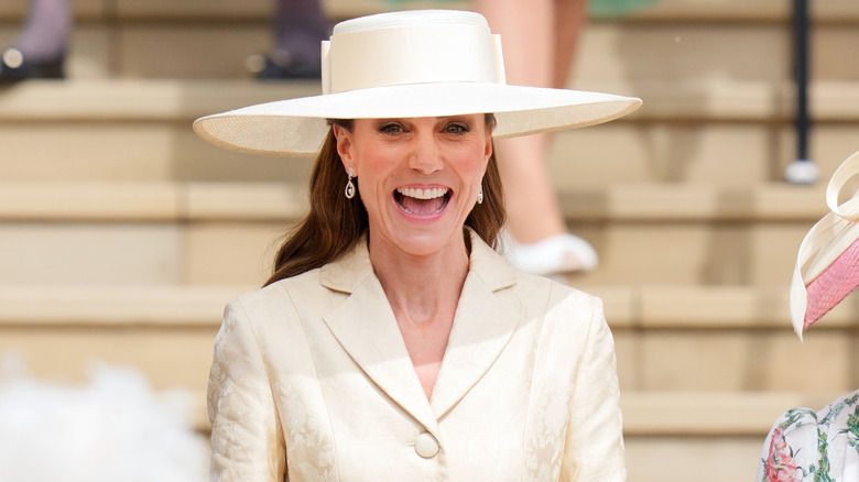 Kate Middleton smiles while wearing a pale-yellow outfit with a matching hat