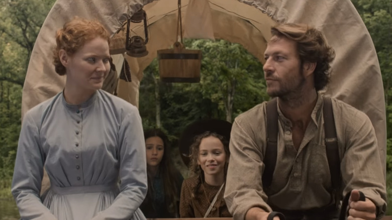 Luke Bracey and Crosby Fitzgerald looking at each other at the front of a covered wagon with characters Laura and Mary behind them in Netflix's 'Little House on the Prairie.'