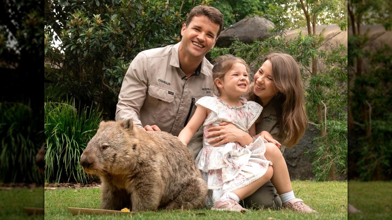 Bindi Irwin holding her daughter posing next to her husband and a wombat.