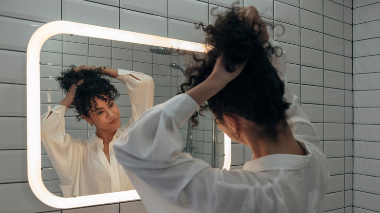 woman creating messy bun in mirror