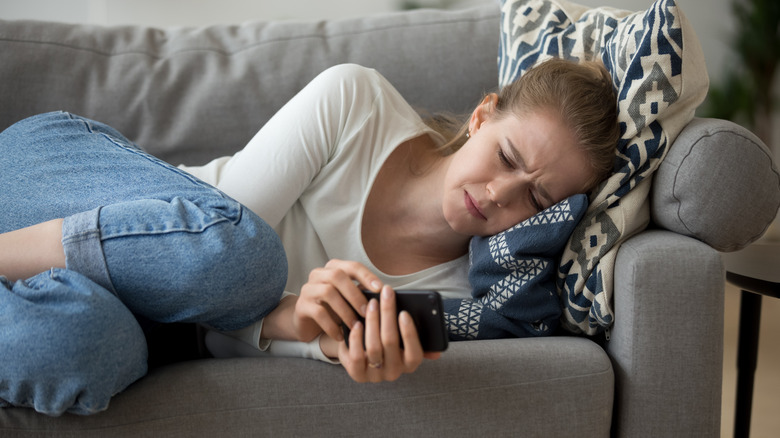 Sad woman lying on a couch texting