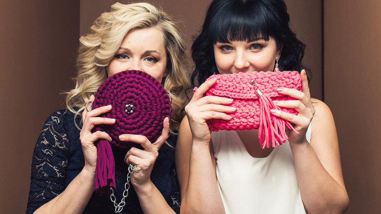 Two women hold up crocheted bags at stylish event