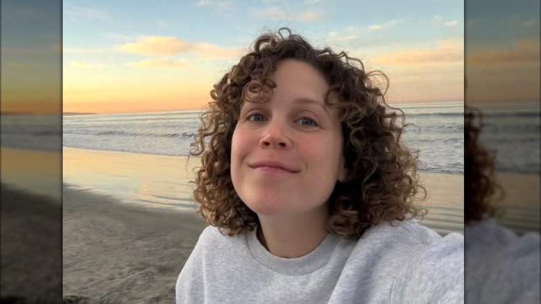 Erin Krakow poses for a sunrise selfie on the beach while sporting a grey sweatshirt and her natural curls