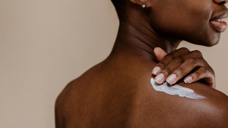 dark skinned woman applying cream to back