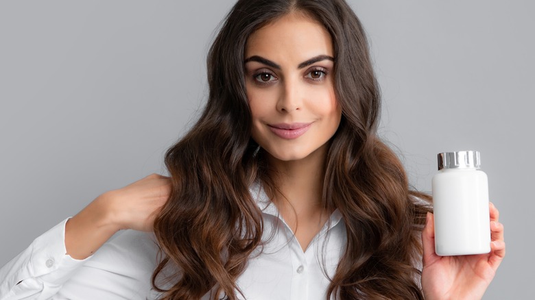 woman holding a bottle of vitamins while showing off hair