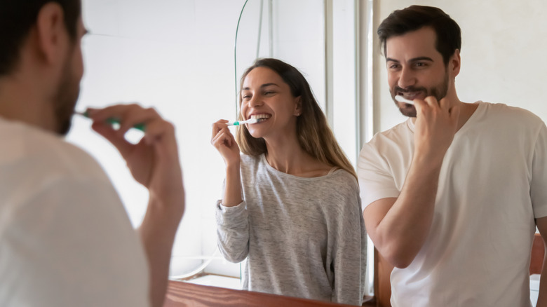 man and woman brushing teeth in mirror