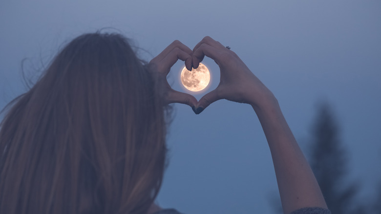 Woman making heart symbol over full moon