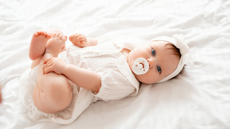 A newborn baby pictured with a headband and pacifier