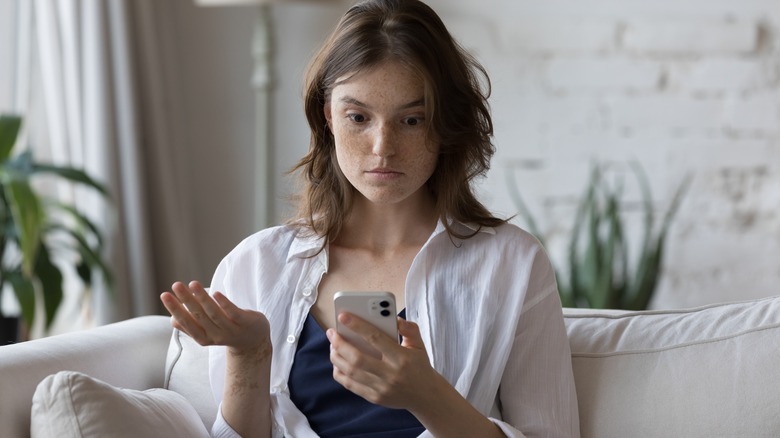 Woman gestures at phone in confusion 