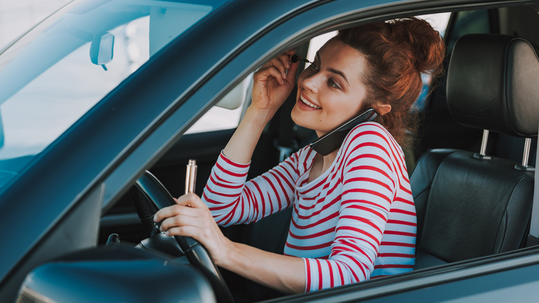 woman putting on makeup on phone and driving