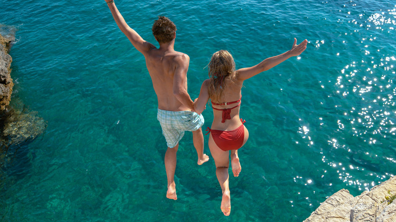 Couple jumping off cliff into ocean