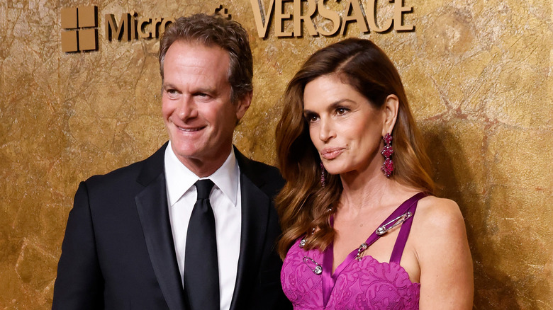 Rande Gerber in a black suit posing with Cindy Crawford wearing a pink dress at a red carpet event.
