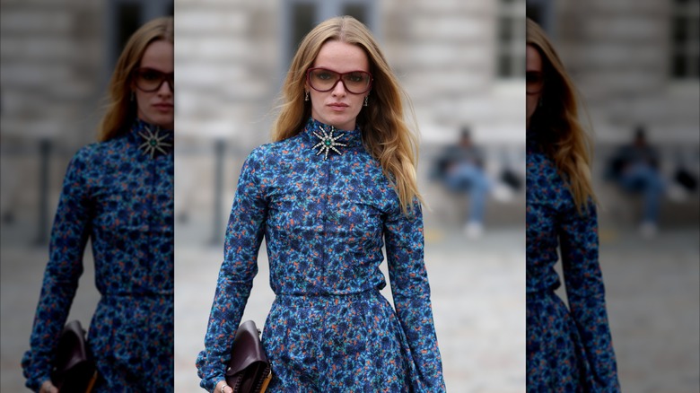 A blond girl wearing a floral blue dress and an embellished brooch