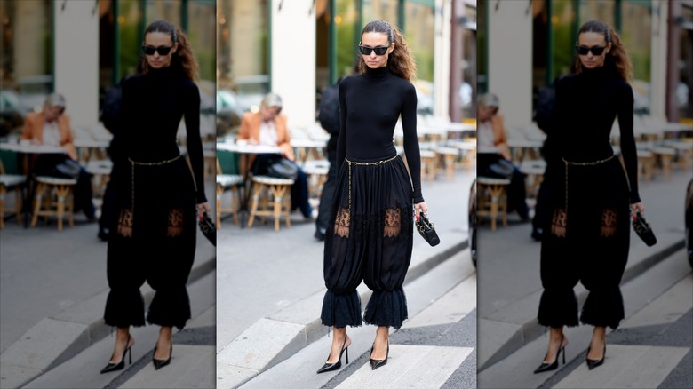 A brunette girl wearing a gold chain belt with black pantalons and a black turtleneck