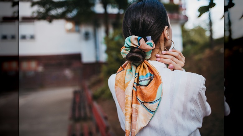 A brunette woman wearing her hair in a bun with a bandana-style scrunchie