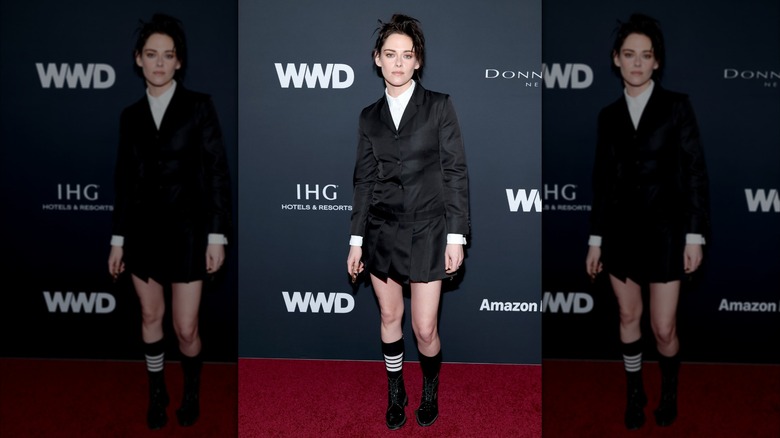 Kristen Stewart wearing a black jacket dress with black shoes at a red carpet event.