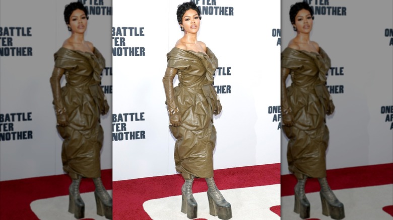 Teyana Taylor posing on a red carpet wearing an olive leather dress with platform boots.