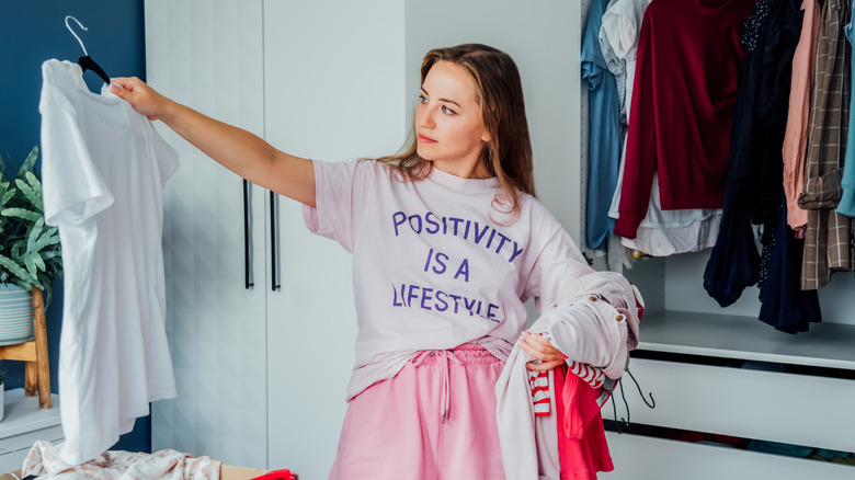 A woman considering clothes as she cleans out her closet.