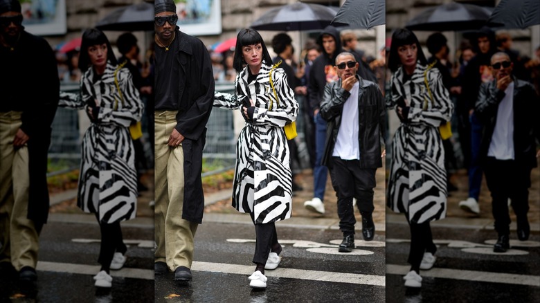A woman during Paris Fashion Week 2024 wears a black and white striped raincoat with white slip-on loafers.
